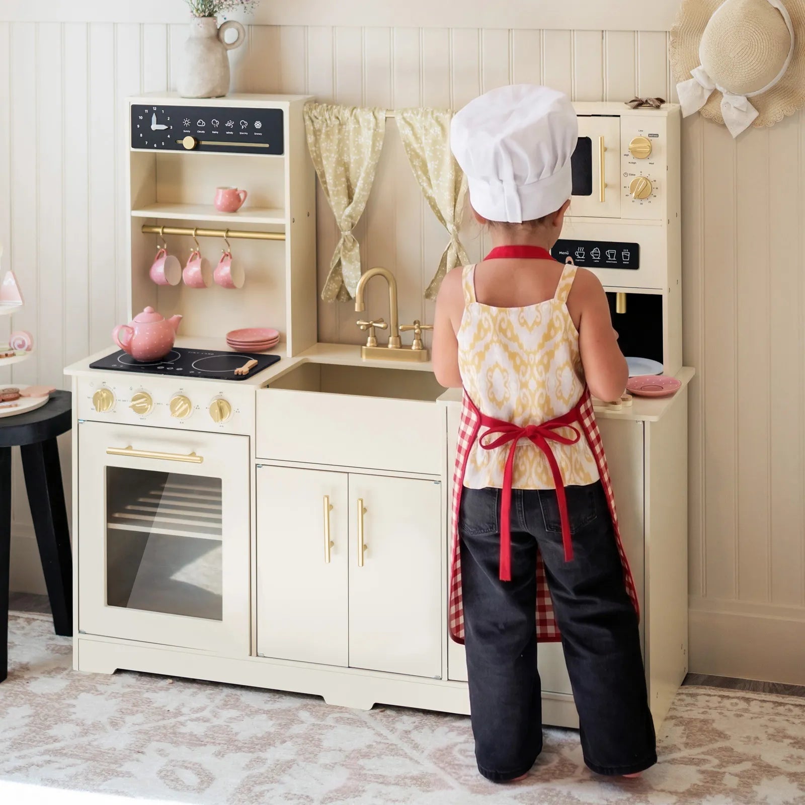 Child in a chef's outfit playing in a toy kitchen set
